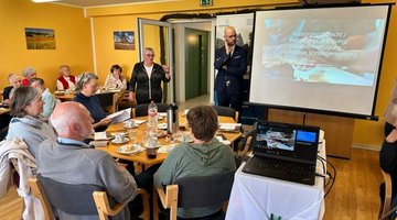 Rund 40 Teilnehmer sitzen bei einer Vorsorgeveranstaltung in der Seniorenpension "Ostseestrand", während Herr Schinschke und Frau Mehl die Vorsorgeveranstaltung begrüßen.