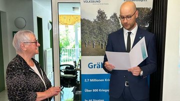 Herr Schinschke ehrt Frau Mehl mit der goldenen Ehrennadel des Volksbundes und verliest den Text der Urkunde